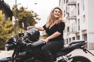 Orta yaşlı, motosikletli bir kadın modern bir motosiklete biniyor.