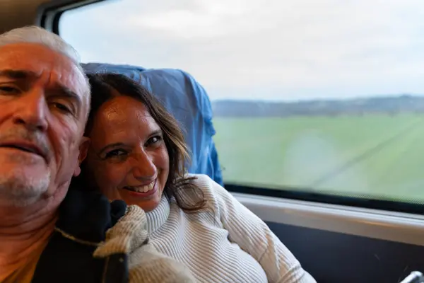 Happy middle aged couple taking a selfie sitting on a train having fun next to the window on vacation - Transportation and vacation concept.