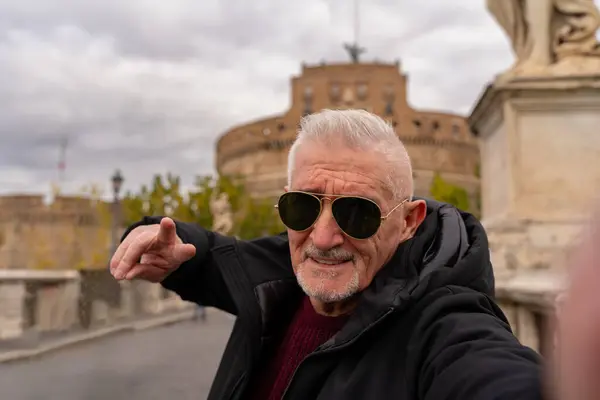 happy middle aged man on vacation taking a selfie in front of castel sant\'angelo fortress in rome - fun and vacation concept.