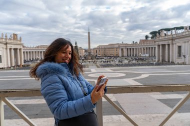 Roma 'daki San Pietro Meydanı' nın önünde cep telefonu kullanan orta yaşlı mutlu bir turist. Seyahat ve eğlence kavramı.