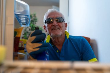 Orta yaşlı bekar adam buzdolabını neşeyle temizliyor. Ev aletinin içinden bakıyor.