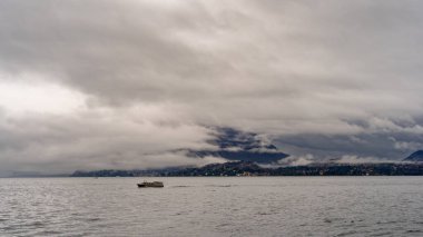 Yağmurlu bir günde Maggiore Gölü 'nün panoramasında kıyı şeridinin bir kısmını yoğun alçak bulutlar kaplıyor. Seyahat ve tatil kavramı.