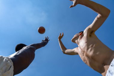 İki genç çok ırklı basketbolcu güneşli bir yaz günü, aşağıdan çekilen suni çim sahada karşı karşıya.