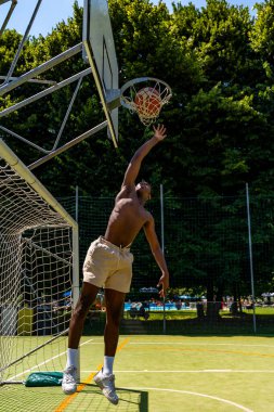 Genç Afro-Amerikan basketbol oyuncusu suni çim üzerinde atlarken güneşli bir yaz gününde sahada.