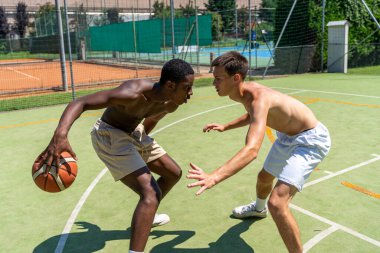 İki genç çok ırklı basketbolcu güneşli bir yaz gününde suni çimlerin üzerinde karşı karşıya gelir.