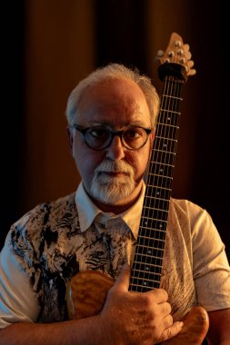Orta yaşlı profesyonel gitarist gitar koleksiyonunun ortasında stüdyosunda poz veriyor.