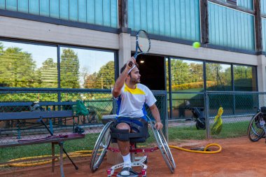 Tekerlekli sandalyedeki engelli tenisçi açık hava kil kortunun kenarında dinleniyor.