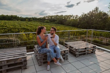 Genç şarap üreticileri sonbaharda üzüm bağlarıyla çevrili bir bardaktan kırmızı şarap tadıyorlar.