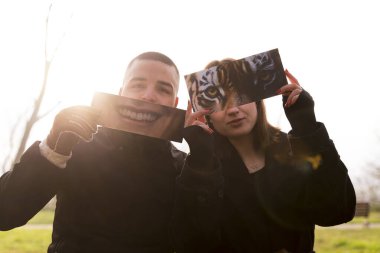 İki genç aşığın portresi, kışın bir halk parkında kısmen yüzlerini kaplayan fantezi resimlerini göstererek eğleniyor.