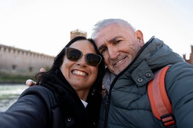 Güzel orta yaşlı çift tatilde. Verona 'daki ünlü scaligero köprüsünde selfie çekiyorlar. Tatil ve eğlence konsepti.
