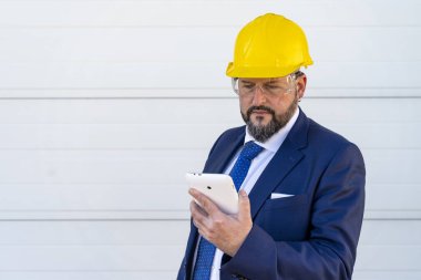 Sakallı iş adamı dışarıda cep telefonu kullanıyor koruyucu sarı kask ve şeffaf iş gözlüğü takıyor.