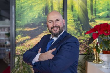 Ofiste çalışırken kameraya bakıp gülümseyen sakallı zarif iş adamının portresi.