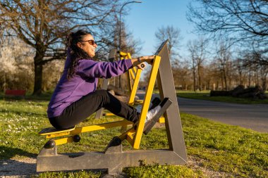 Spor giyimli orta yaşlı güzel bir kadın açık hava parkında spor eğitimi alıyor.