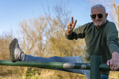Spor giyimli orta yaşlı bir sporcu açık hava parkında metal bir çitin üzerinde geriniyor.
