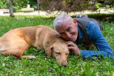 Orta yaşlı bir adam parkın çimlerinde uzanmış köpeğiyle mutlu anların tadını çıkarıyor.