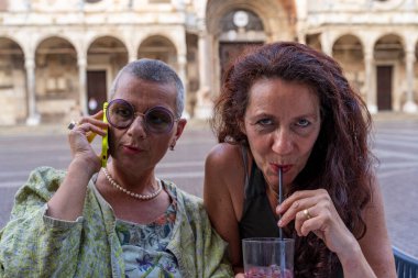 Güzel orta yaşlı kadın çiftin portresi. Tarihi meydandaki açık kafeterya masasında içki içip telefon kullanıyorlar.