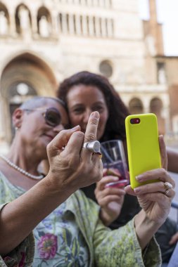 Güzel orta yaşlı bir çiftin portresi, tarihi bir meydanda açık bir masada cep telefonuyla selfie çekerken eğleniyor.