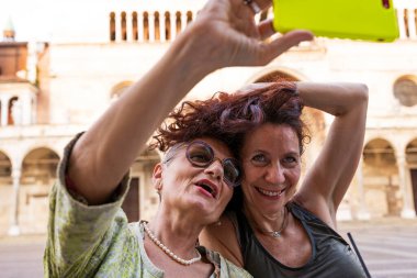 Güzel orta yaşlı bir çiftin portresi, tarihi bir meydanda açık bir masada cep telefonuyla selfie çekerken eğleniyor.