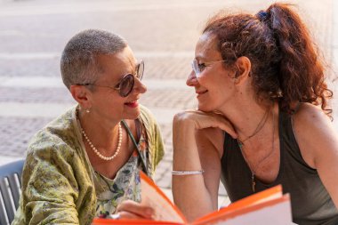 Güzel orta yaşlı lezbiyen çift, tarihi bir meydanda açık bir kafe masasında sevişiyor.