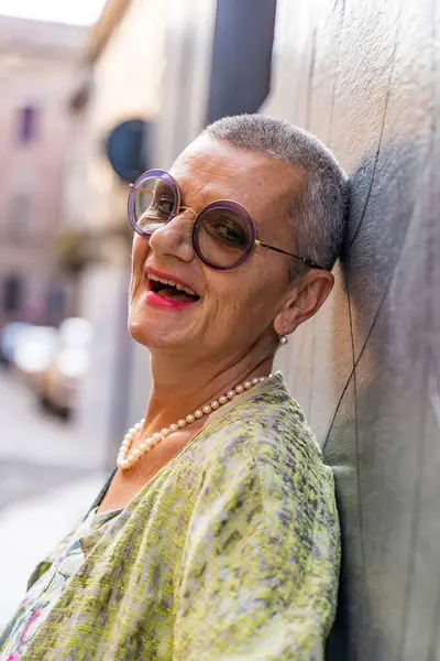 Siyah duvara yaslanmış kameraya bakan zarif, olgun bir kadının portresi.