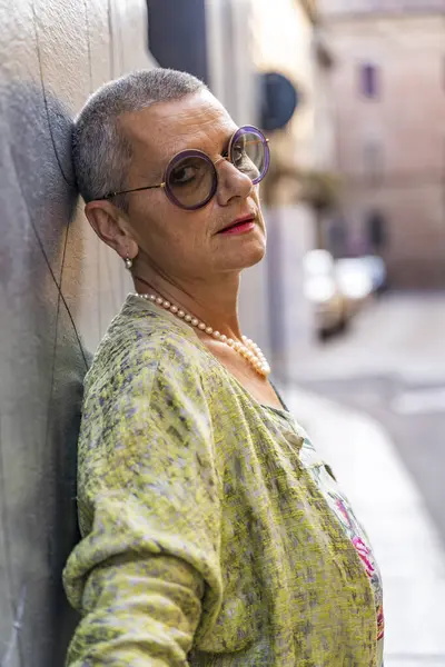 Sokakta siyah duvara yaslanmış kameraya bakan güzel olgun bir kadının portresi.