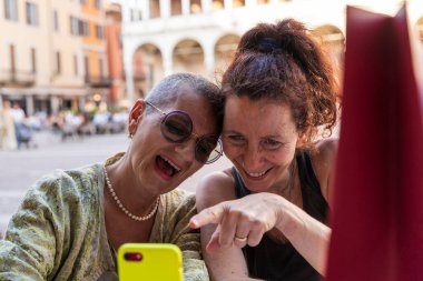 Tatilde olan güzel bir çift orta yaşlı kadının portresi. Açık bir masada oturmuş cep telefonuna bakarken eğleniyorlar.