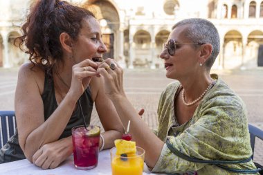 Güzel bir çift orta yaşlı bayan arkadaş tarihi bir meydanda açık bir kafede oturmuş aperatifin tadını çıkarıyorlar.