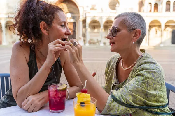 Güzel bir çift orta yaşlı bayan arkadaş tarihi bir meydanda açık bir kafede oturmuş aperatifin tadını çıkarıyorlar.