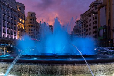 Valencia meydanındaki tarihi binalarla çevrili renkli ışıklarla dolu bir çeşme.
