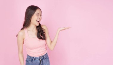 Heyecanlı Asyalı kadın elini kaldırdı ve pembe arka planda durdu. Kendinden emin gülümseyen genç kız, elinde fotokopi alanı gösteriyor. Ürünü izole edilmiş halde sunuyor. Reklam sunumu konsepti.