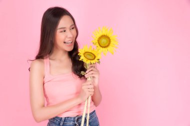 Elinde taze ayçiçeği tutan neşeli Asyalı kadın pembe arka planda duruyor. Heyecanlı Asyalı genç kız gündelik görünüşlü ayçiçeği çiçeği elinde gülümsüyor izole edilmiş pastel arka planda fotokopi alanı ile rahatla. 