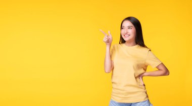 Neşeli heyecanlı Asyalı kadın parmak uçlarını ürünle ya da izole edilmiş sarı arka planda duran boş fotokopi alanıyla gösterir. Model genç kız gülme promosyonu. Reklam sunma konsepti