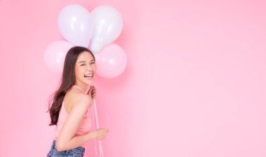 Excited cheerful asian woman holding balloons and hands beside mouth smiling with toothy standing over isolated pink background. Joyful teenager girl with pastel balloons shocked  amazed expression.