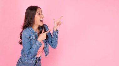 Cheerful excited asian woman use finger pointing to side with product or empty copy space standing over isolated pink background. Model young girl laughing promotion. Advertisement presenting concept