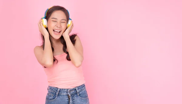 幸せなアジアの女性は ピンクの背景に立っているプレイリストをリスニングヘッドフォンを着用しています チル若い女の子は 孤立したパステルバック上のイヤホンソングミュージックでサウンドメロディラジオを聞きます ホビー ホビー — ストック写真