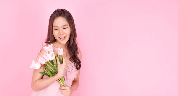 陽気な驚きのアジアの女性は ピンクの背景にコピースペースでリラックスして立っている花のチューリップを保持しています グラマーの興奮した若い女の子は 孤立したピンクの背景に花の笑顔を保持するドレスを着ています — ストック写真