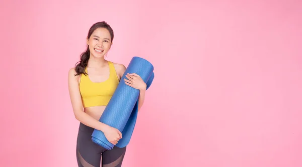 Excited sporty asian women wear sports wear holding rush mat yoga in hand standing copy space on pink background. Cheerful positive slim body young girl hold yoga mat smiling over isolated. Exercise