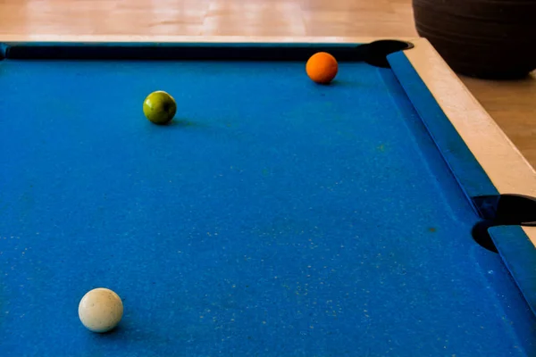 A close-up shot of a pool table with a white ball, an orange and a green apple. The white ball is near the center of the table, ready to hit the orange and the apple, which are near the hole. The orange and the apple are ripe and juicy, creating a co