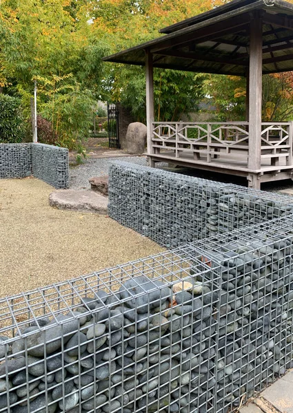 Gabions in the autumn garden. Gabions and Japanese tea gazebo on a wooden platform in the garden. Gabions and boulders on a flat area of fine gravel. Appeltern, Netherlands, October 12, 2022. Appeltern is the Netherlands\' largest garden idea park