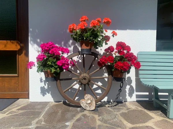 Flowers on the porch. Beautiful front door with flowers. Decorations made from wagon wheel and pelargonium. Tirol, Austria.