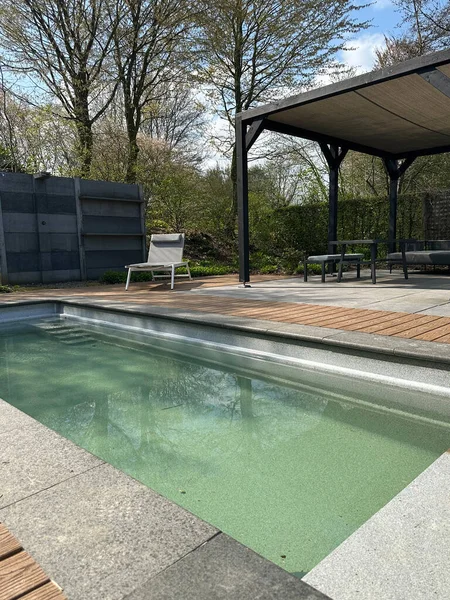 Swimming pool in garden. Modern terrace with pool, aluminum pergola and deck chair. Wooden decking. Appeltern, Netherlands, April 09, 2023: The garden inspiration park for the whole family