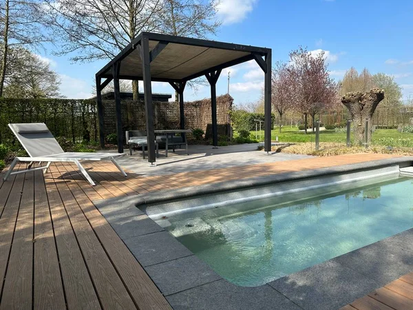 Swimming pool. Modern terrace with pool, aluminum pergola and deck chair. Wooden decking. Appeltern, Netherlands, April 09, 2023: The garden inspiration park for the whole family