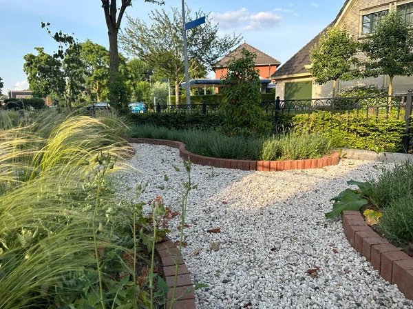 Modern front garden with light grey gravel.  Flower beds and brick borders. In the foreground Stipa tenuissima (Mexican feather grass)
