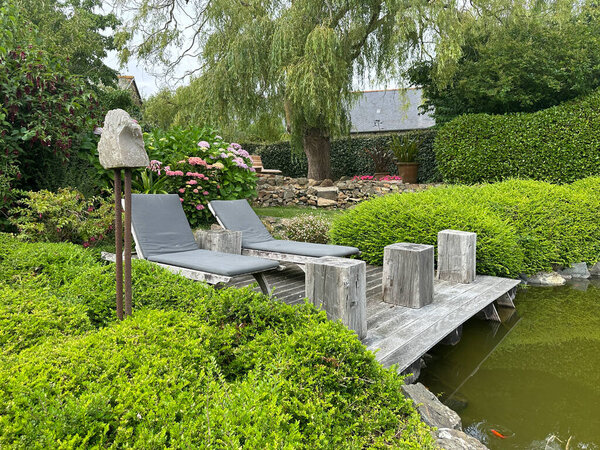 шезлонги на деревянной палубе у пруда. Пышная растительность и цветущие растения