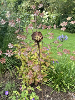 Decorative metal flower sculpture with intricate details in a lush green garden. The weathered metal blends harmoniously with its natural surroundings. Gardens 'Jardin du Rossignol', France clipart