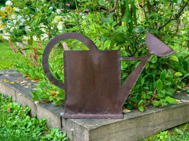 Paslı metal sulama, ahşap kenarlı bir çiçek tarhında heykel yapabilir. Bahçenin doğal güzelliğini arttıran eşsiz bir aksan. Jardin du Rossignol Bahçeleri. Willeman, Fransa