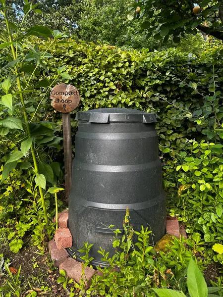 Sebze bahçesindeki gübre kutusu. Yeşilliklerle çevrili plastik bir konteynır. Ahşap levhada gübre yığını anlamına gelen gübre halkası yazıyor. Heemtuin Malden, Hollanda 'da bir halk ekolojik bahçesi.