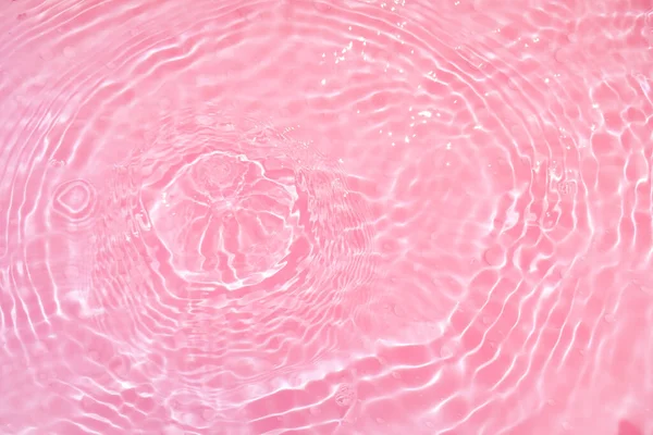 Defocus blurred transparent pink colored clear calm water surface texture with splashes and bubbles. Trendy abstract nature background. Water waves in sunlight with copy space. Pink watercolor shining