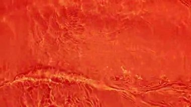Defocus bulanık kırmızı şeffaf, berrak, durgun su yüzeyi dokusu sıçrama ve kabarcıklarla bulanıklaştırılmış. Moda soyut doğa geçmişi. Güneş ışığında su dalgaları. Kırmızı su arka planda parlıyor.