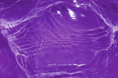 Defocus bulanık, şeffaf mor renkte berrak, durgun su yüzeyi dokusu sıçrama ve kabarcıklarla bulanıklaştırılmış. Moda soyut doğa geçmişi. Güneş ışığında fotokopi uzayıyla birlikte su dalgaları. Pembe su damlası parlıyor